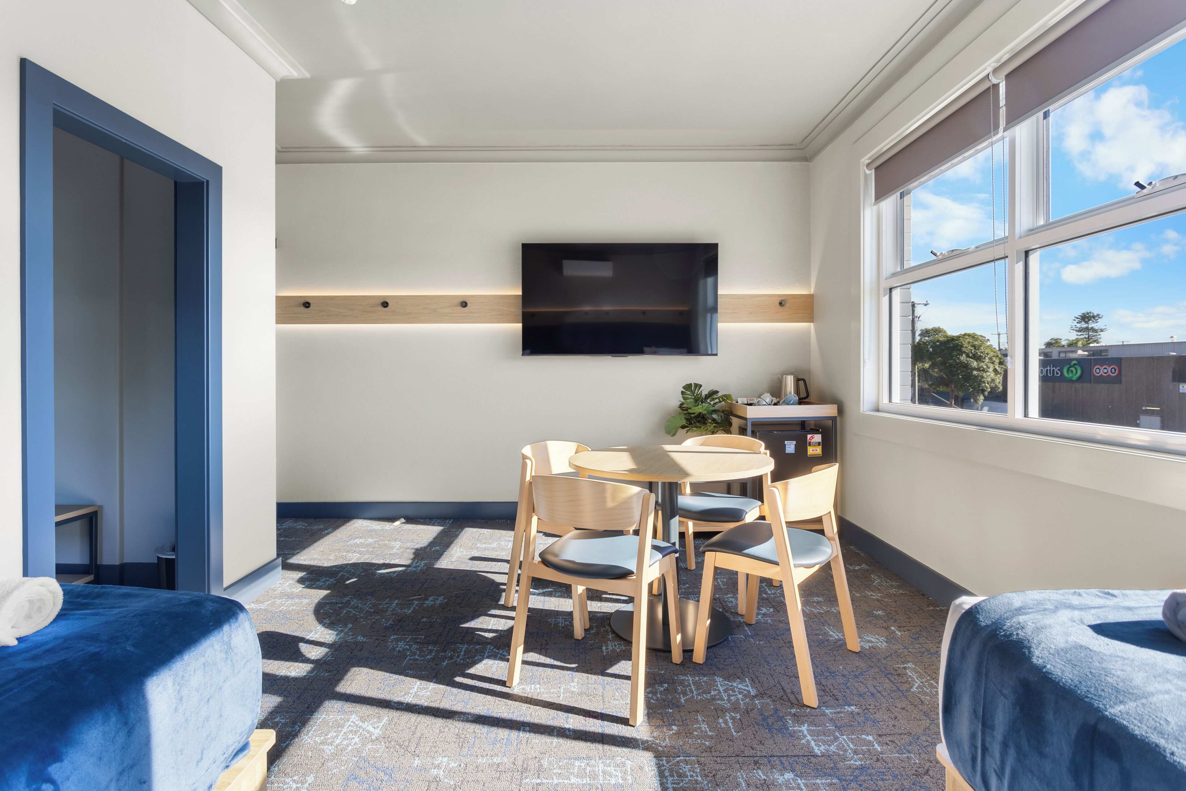 A room with a bed, a desk with a chair, a TV mounted on the wall, and a window with a view of the outside.