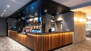 A modern bar area with a wooden counter, overhead lighting, and a tiled wall. - Hotel Jesmond (Jesmond)