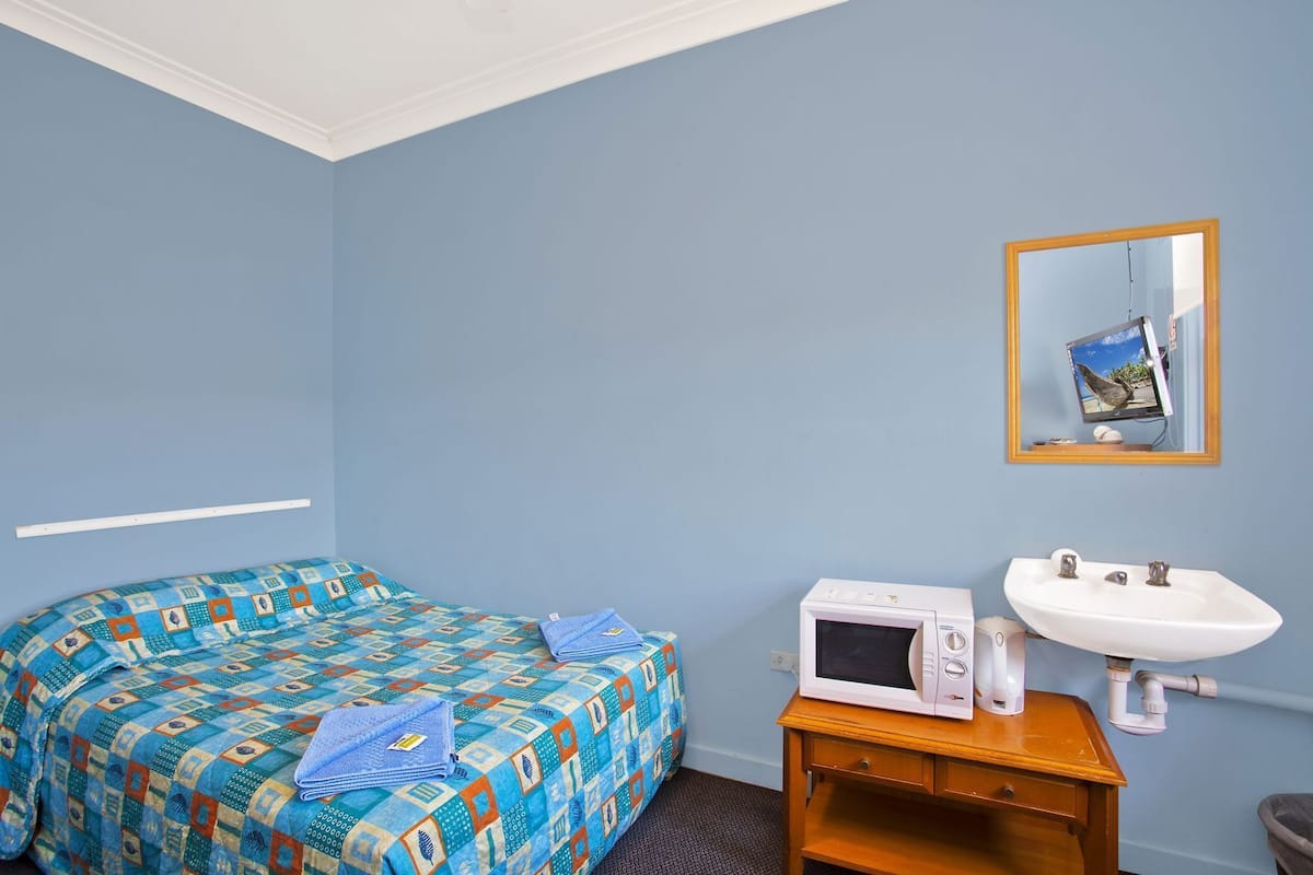 Una habitación con cama, microondas, lavabo y espejo.