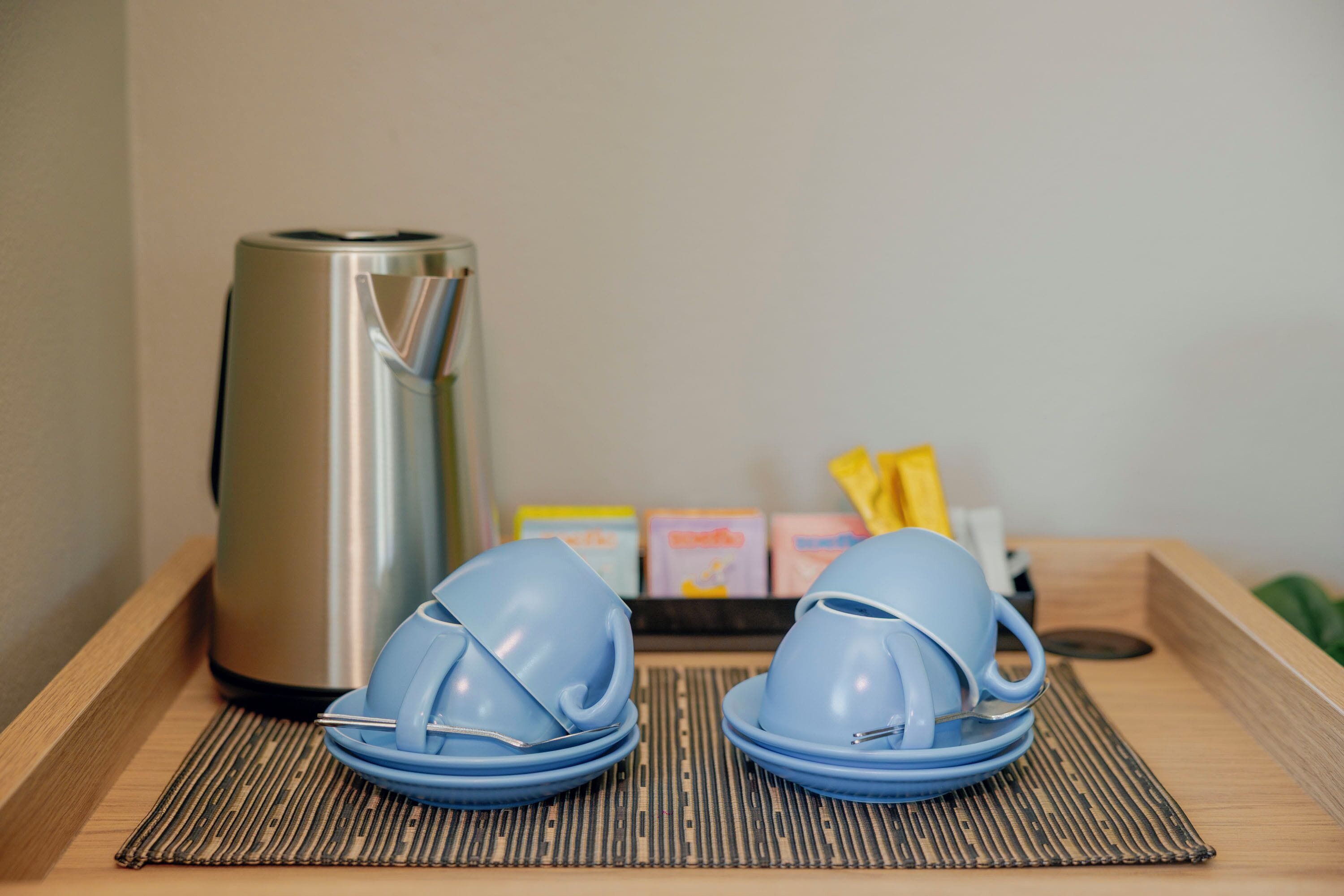 A kitchen area with a stainless steel kettle, blue plates, and a tray with packaged food items.