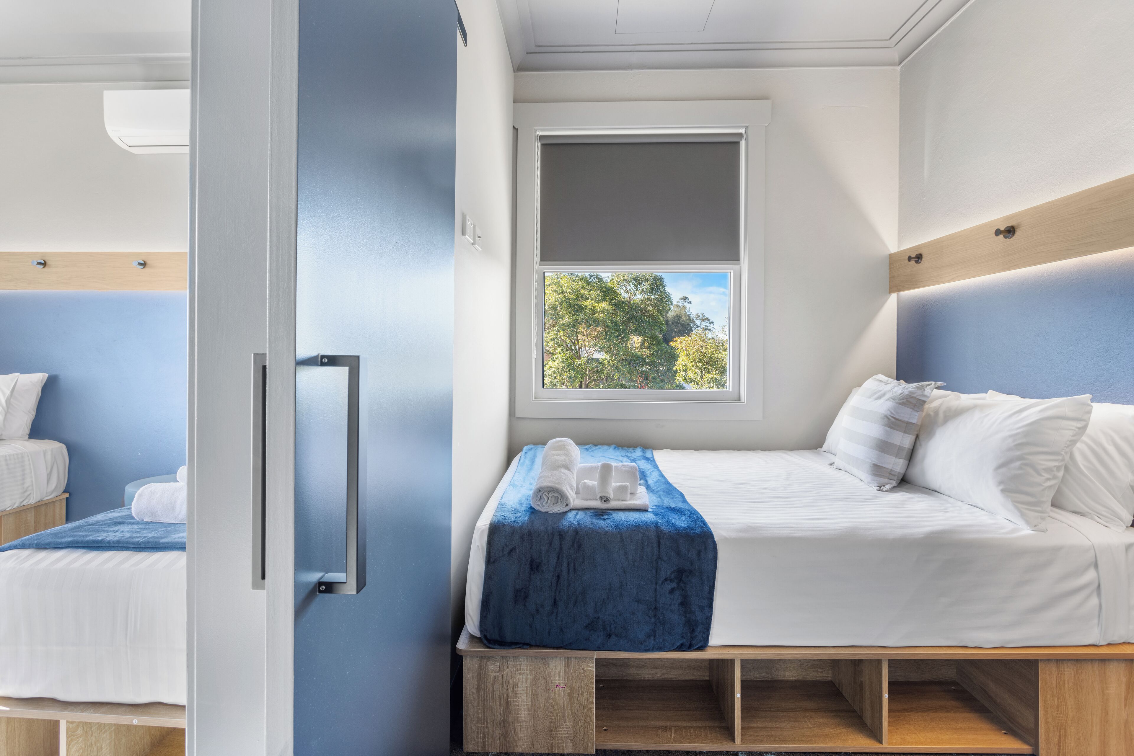 A compact bedroom with a single bed, a small window, and a view of trees outside.