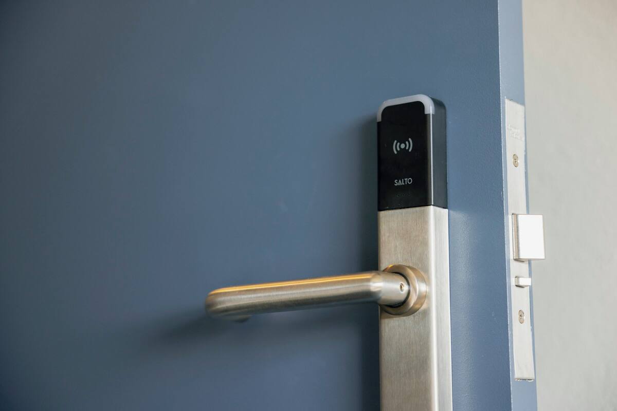 Una puerta con manija metálica y cerradura, un mecanismo de bloqueo, y un pequeño dispositivo electrónico con la etiqueta "SALTO" en el marco de la puerta.
