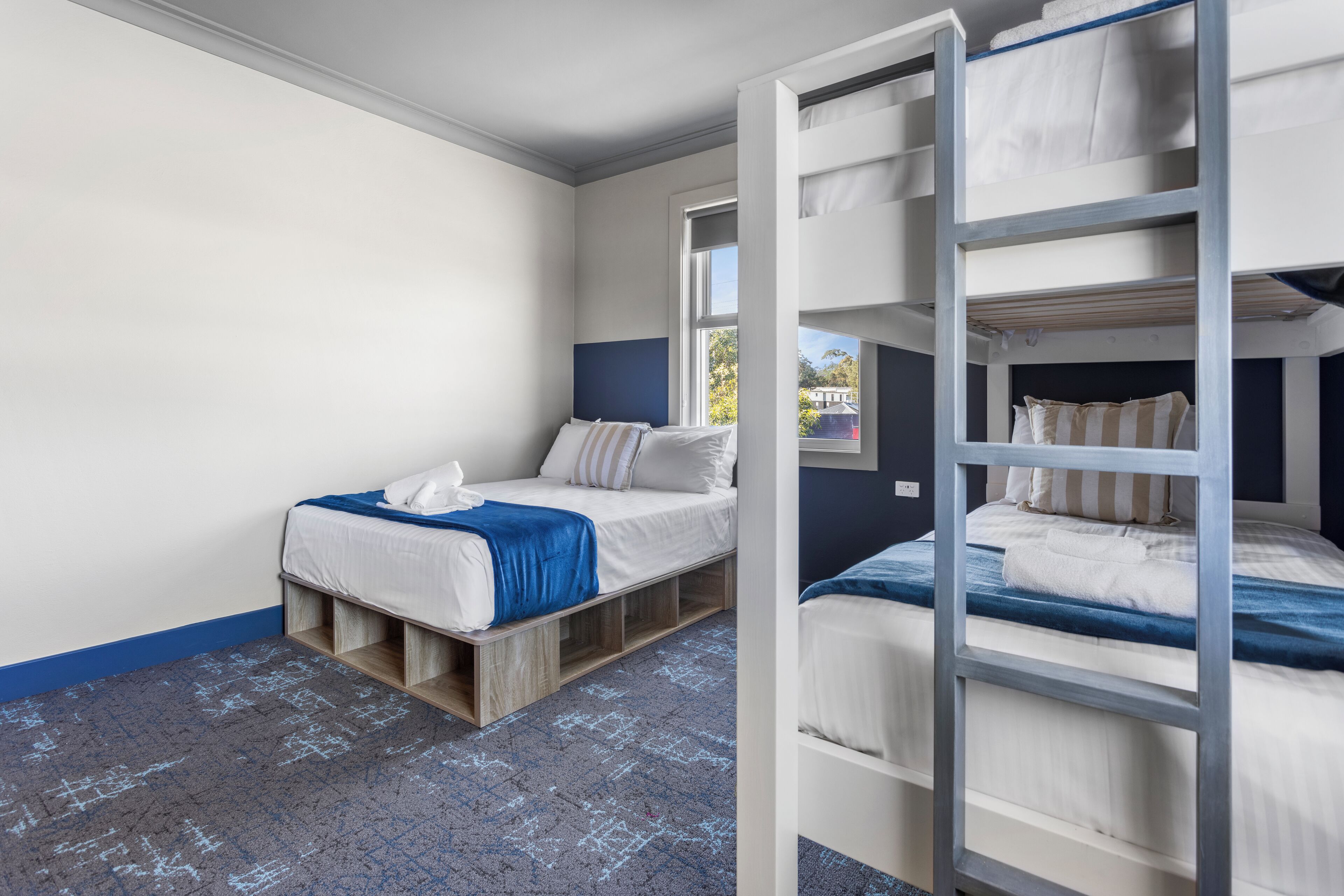 A room with bunk beds, a window, and a blue carpet.