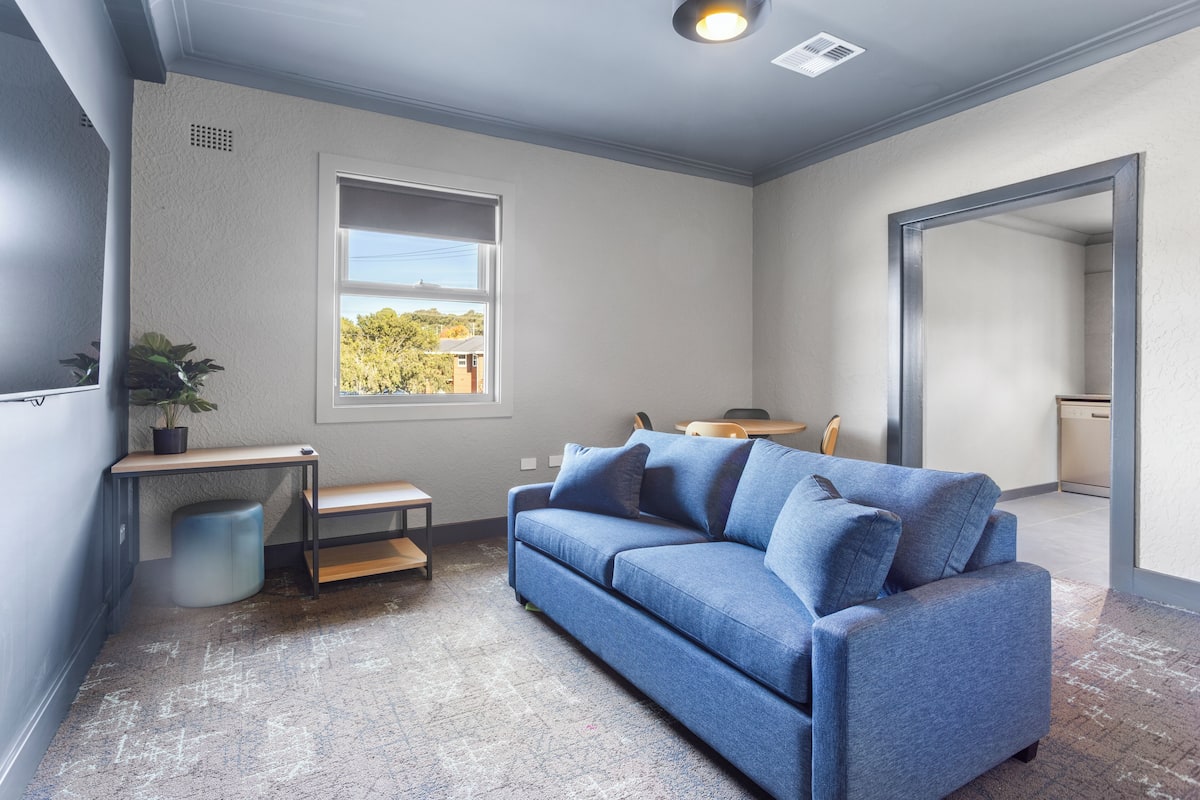 Una sala de estar moderna con un sofá azul, una mesita y un ventanal con vistas.