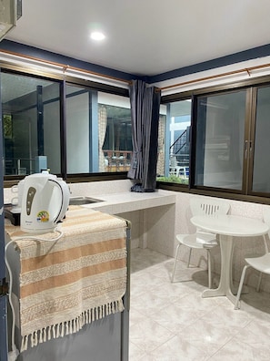 Een kleine kitchenette met een waterkoker, een gestreepte handdoek en een raam met gordijnen.