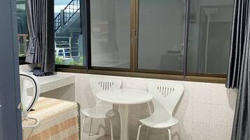 Un pequeño comedor con una mesa redonda y cuatro sillas, una ventana con cortinas y un suelo de baldosas.
