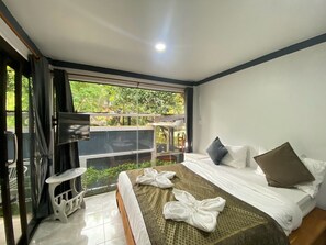 A hotel room with a bed, a small table, and a balcony with a view of greenery. - Chaweng Noi Resort (Koh Samui)