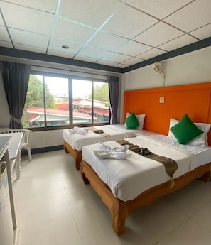 Een hotelkamer met twee bedden, een bureau en een raam met uitzicht op gebouwen.