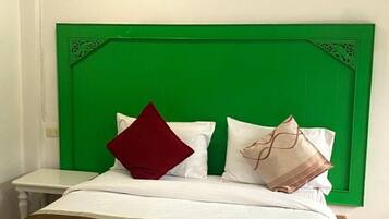 Habitación de hotel con cabecera verde, ropa de cama blanca y una toalla blanca doblada cuidadosamente sobre la cama.