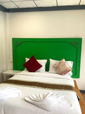 A hotel room with a green headboard, white bedding, and a neatly folded white towel on the bed. - Chaweng Noi Resort (Koh Samui)