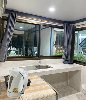 Una cucina compatta con lavello integrato, bollitore e vista su un balcone esterno.