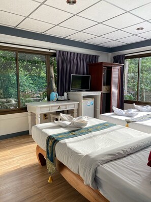 Quarto de hotel com cama, escrivaninha com televisão e janelas amplas.