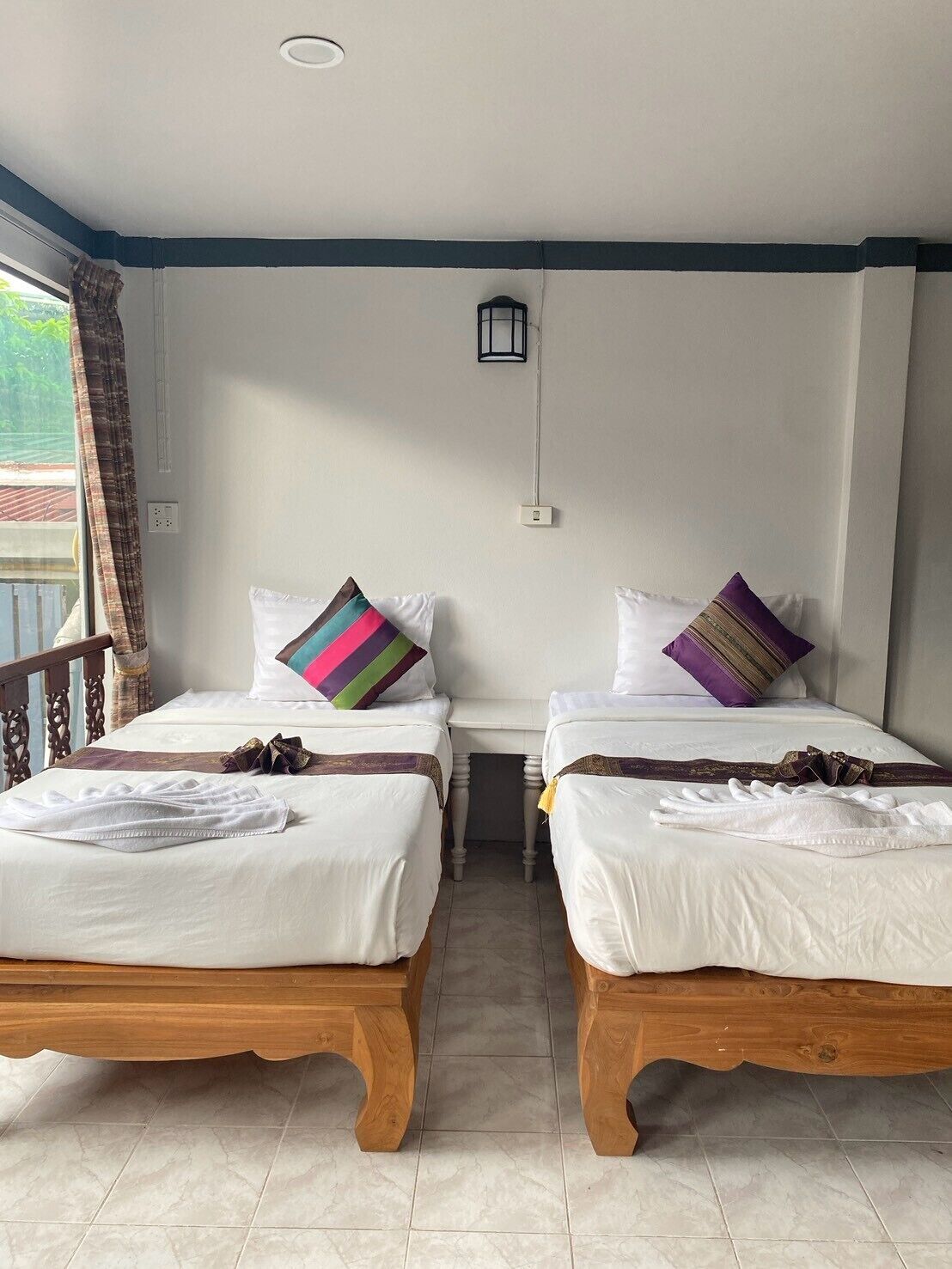 A hotel room with two wooden beds, white linens, and colorful pillows.