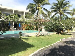 A pool area with a clear view of the surrounding greenery and a building with multiple balconies. - The Living Pool Villas (Koh Samui)