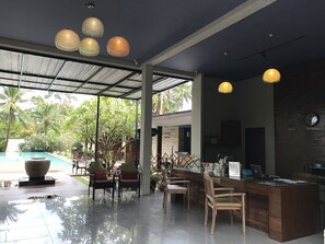 A modern reception area with a pool view, wooden furniture, and hanging pendant lights. - The Living Pool Villas (Koh Samui)