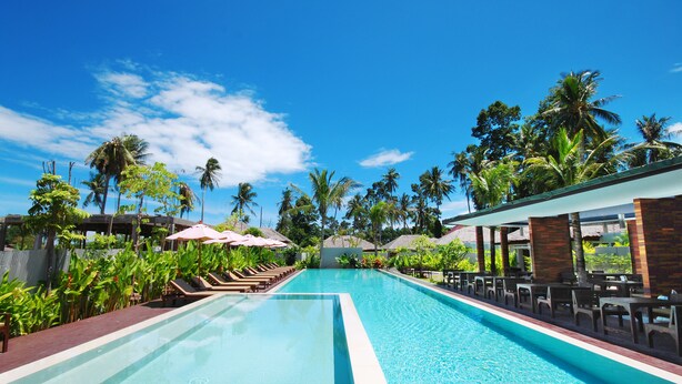 A swimming pool with lounge chairs and umbrellas, surrounded by palm trees and tropical plants. - The Living Pool Villas (Koh Samui)