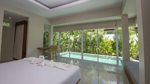 A hotel room with a large bed, a wooden chair, and a view of a swimming pool and lush greenery. - The Living Pool Villas (Koh Samui)
