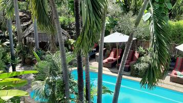 A pool surrounded by lush greenery and palm trees, with a thatched-roof structure in the background.