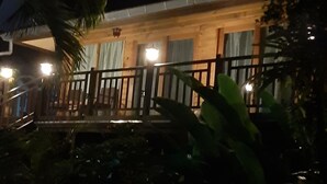 Un edificio de madera con balcón y barandilla, rodeado de follaje.