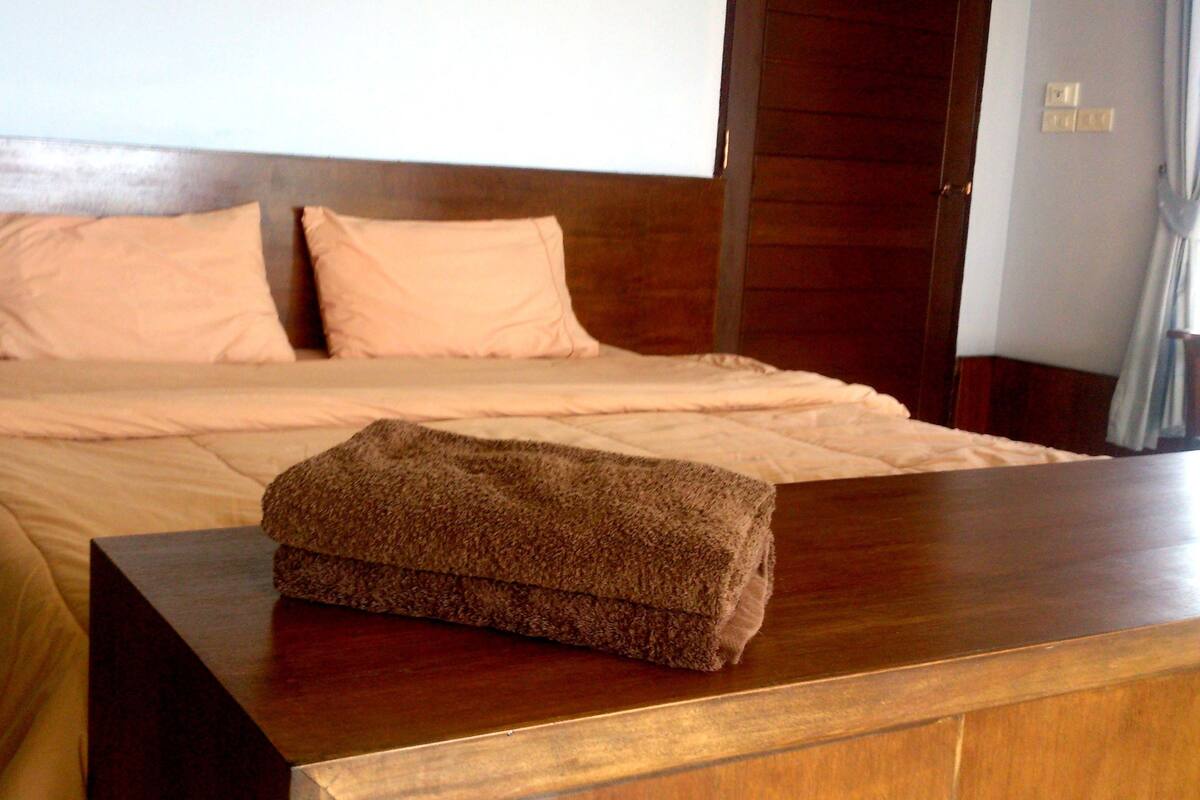 A neatly made bed with a wooden headboard and a brown blanket on a wooden dresser.