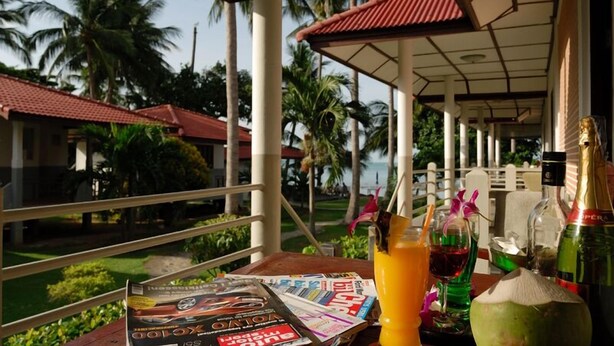 A table with magazines, a bottle of champagne, a glass of orange juice, and a coconut. - Thong Takian Resort (Koh Samui)