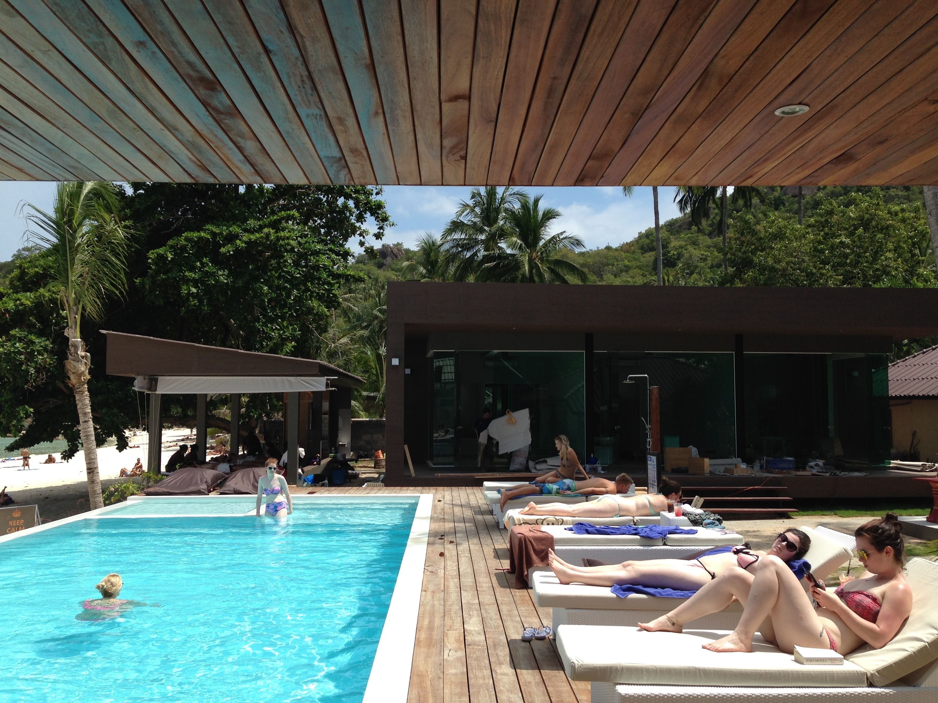 Un área de piscina con sillones de descanso y una terraza techada.