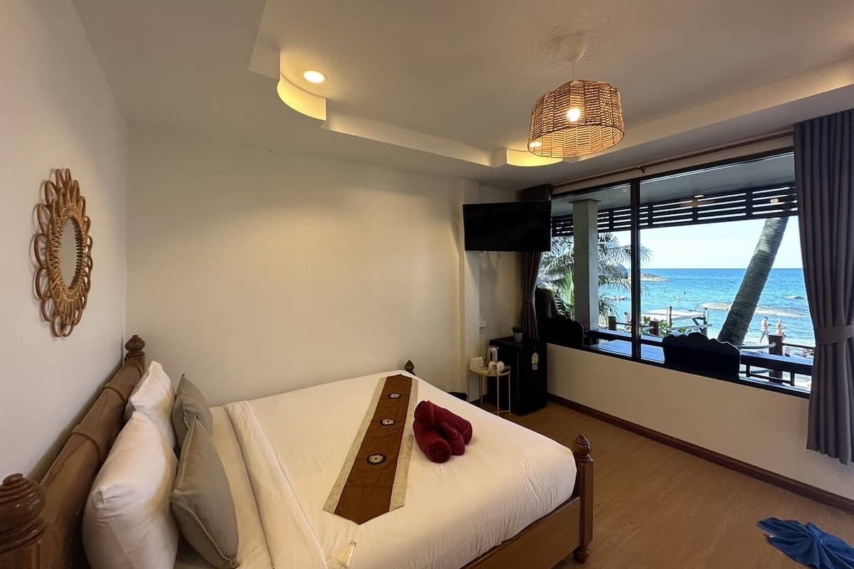 Une chambre à coucher avec un grand lit, une télévision, une fenêtre donnant sur la mer et un miroir décoratif.