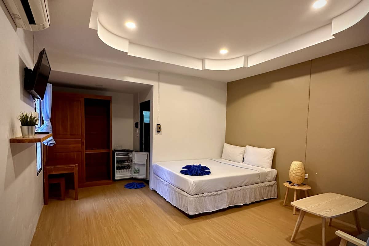 Une chambre à coucher de taille réduite, comprenant un lit, une petite table, une chaise, un téléviseur fixé au mur et une armoire intégrée.