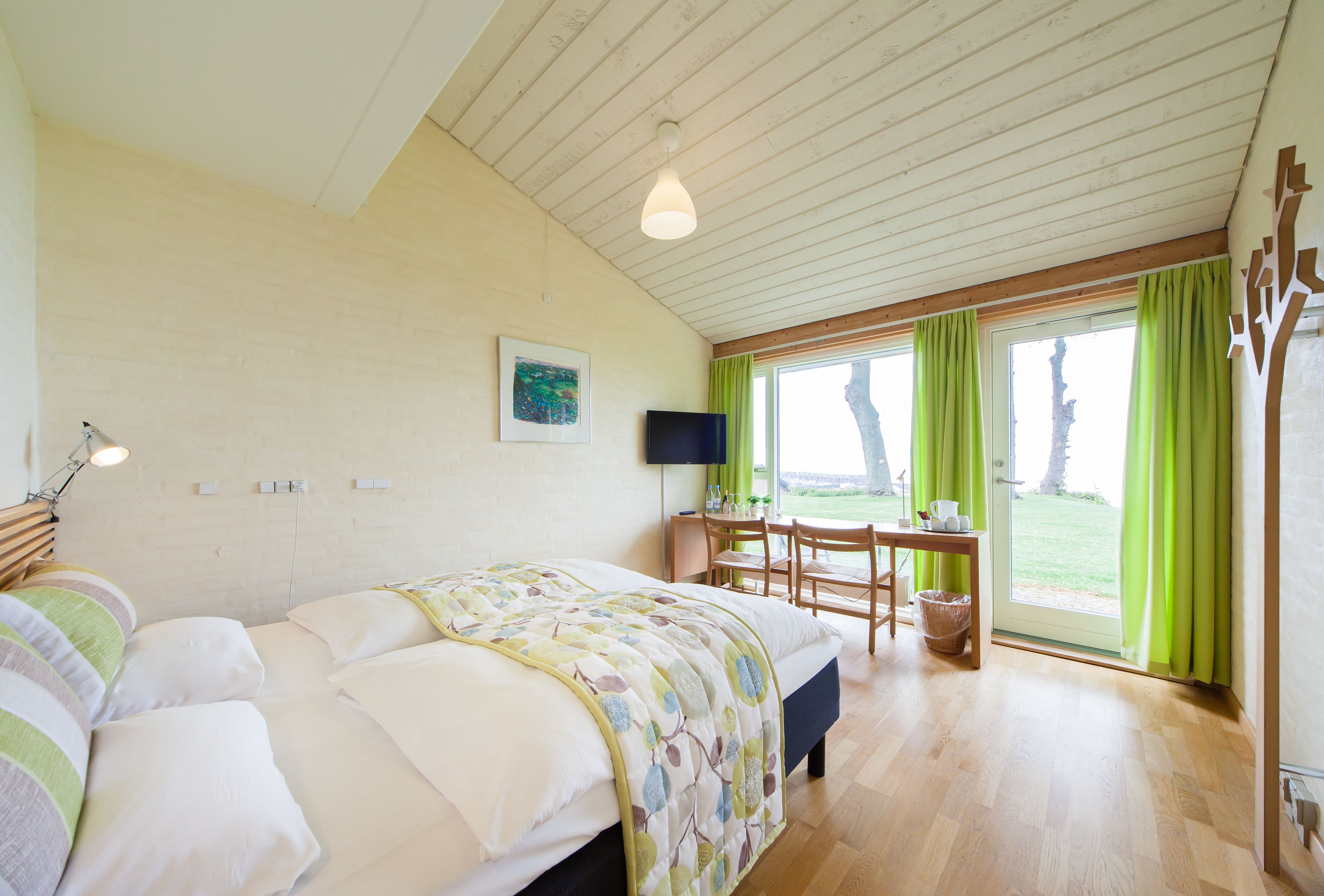 A bedroom with a bed, a desk, and a chair. There is a window with curtains and a view of the outdoors.