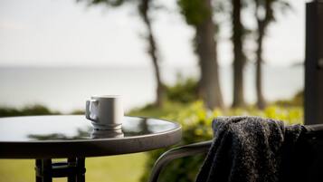 A white mug on a round table with a view of the ocean and palm trees in the background.