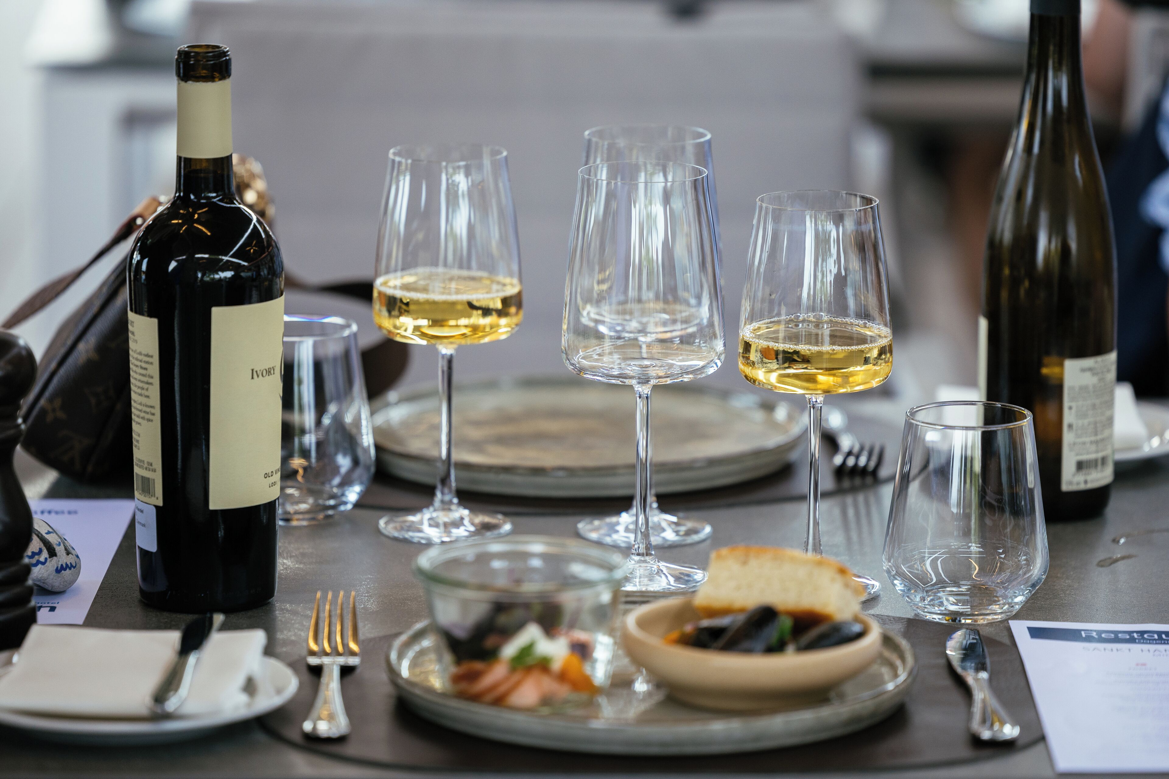 Une table à manger dressée avec des verres à vin, des assiettes, des couverts et une bouteille de vin.