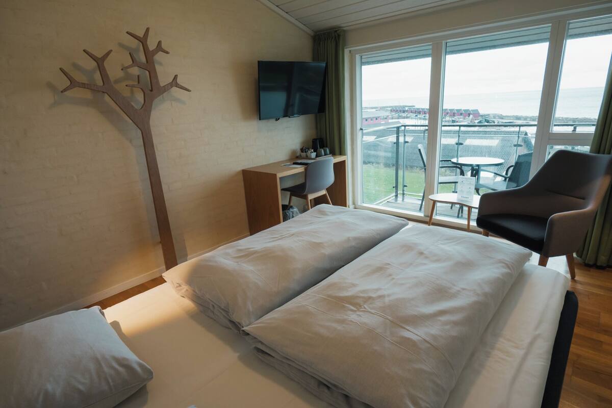Una habitación de hotel con cama, escritorio, televisión y balcón con una silla.