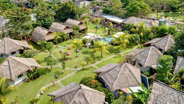 A resort with thatched-roof huts, a swimming pool, and a view of the ocean.