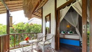 A balcony with wicker chairs and a small table, a bed with a canopy, and a view of greenery.