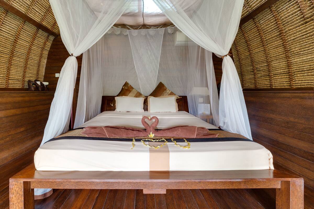 A neatly made bed with white linens, a canopy, and decorative pillows.