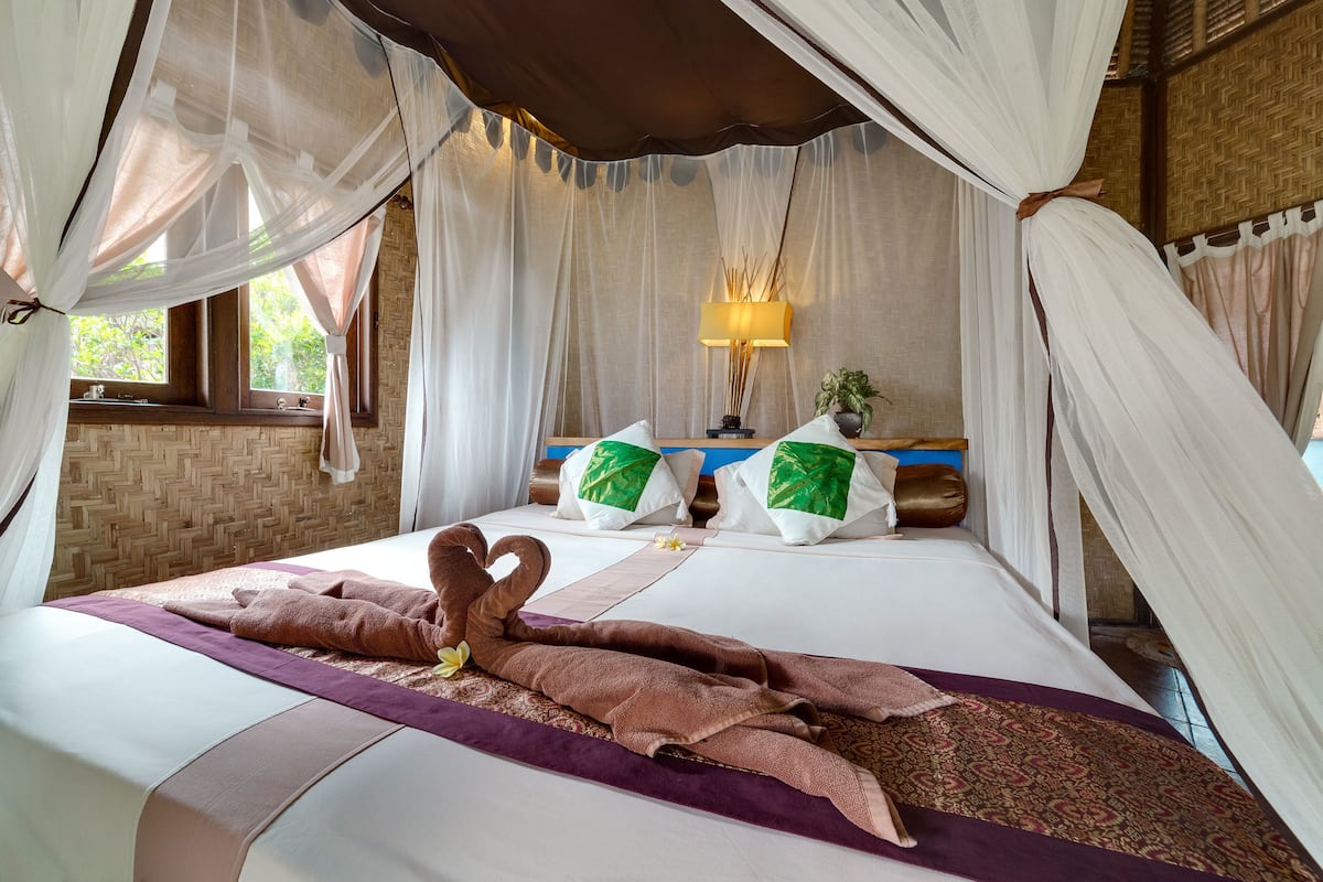 A bed with a canopy, pillows, a bedside lamp, and a towel arrangement.