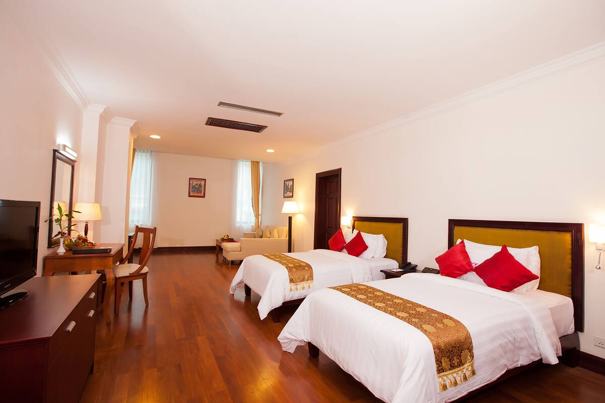 A hotel room with two beds, a desk, a TV, and a chair.
