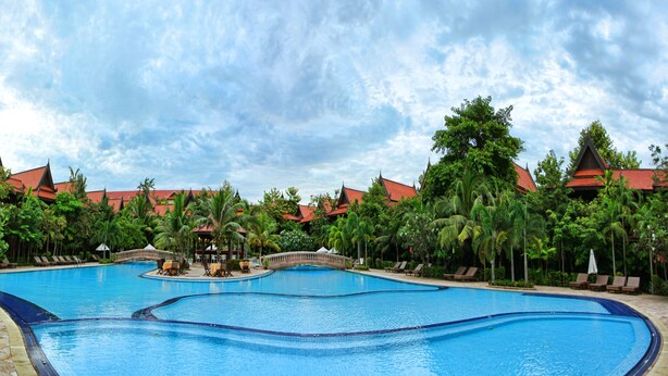 A large swimming pool with a bridge, surrounded by palm trees and buildings with red roofs. - Sokhalay Angkor Residence and Spa (Siem Reap)