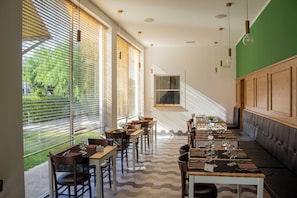 Un restaurant doté de grandes fenêtres, de tables en bois et d’un mur d’accent de couleur verte.