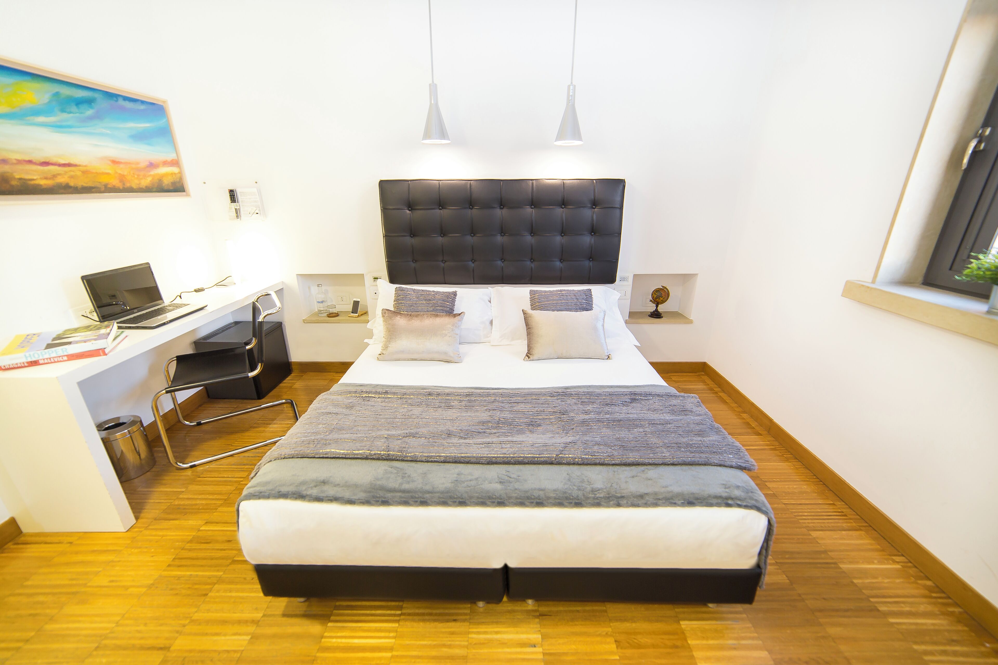 A bedroom with a bed, desk, and a painting on the wall.