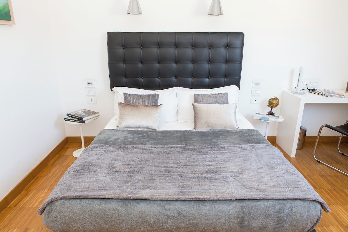 A bed with a black headboard, white pillows, and a grey blanket.