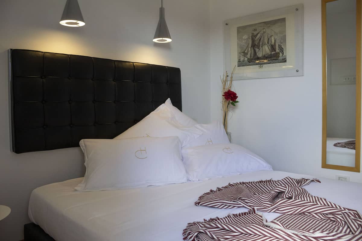 A neatly made bed with white bedding and a zebra-striped throw blanket, a black upholstered headboard, and a framed artwork on the wall.