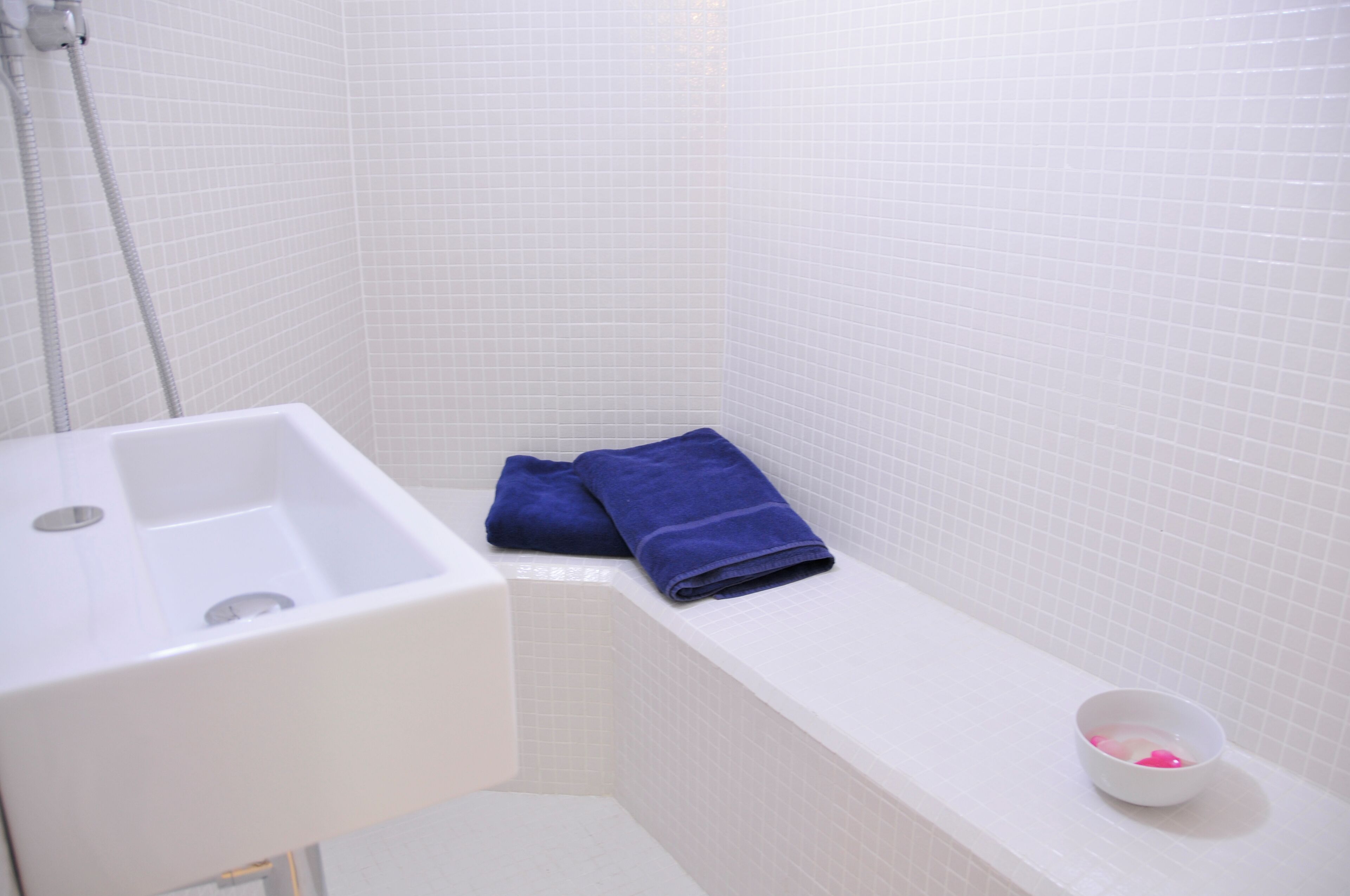 A bathroom with a white sink, a bathtub, and a small white basin with pink items.