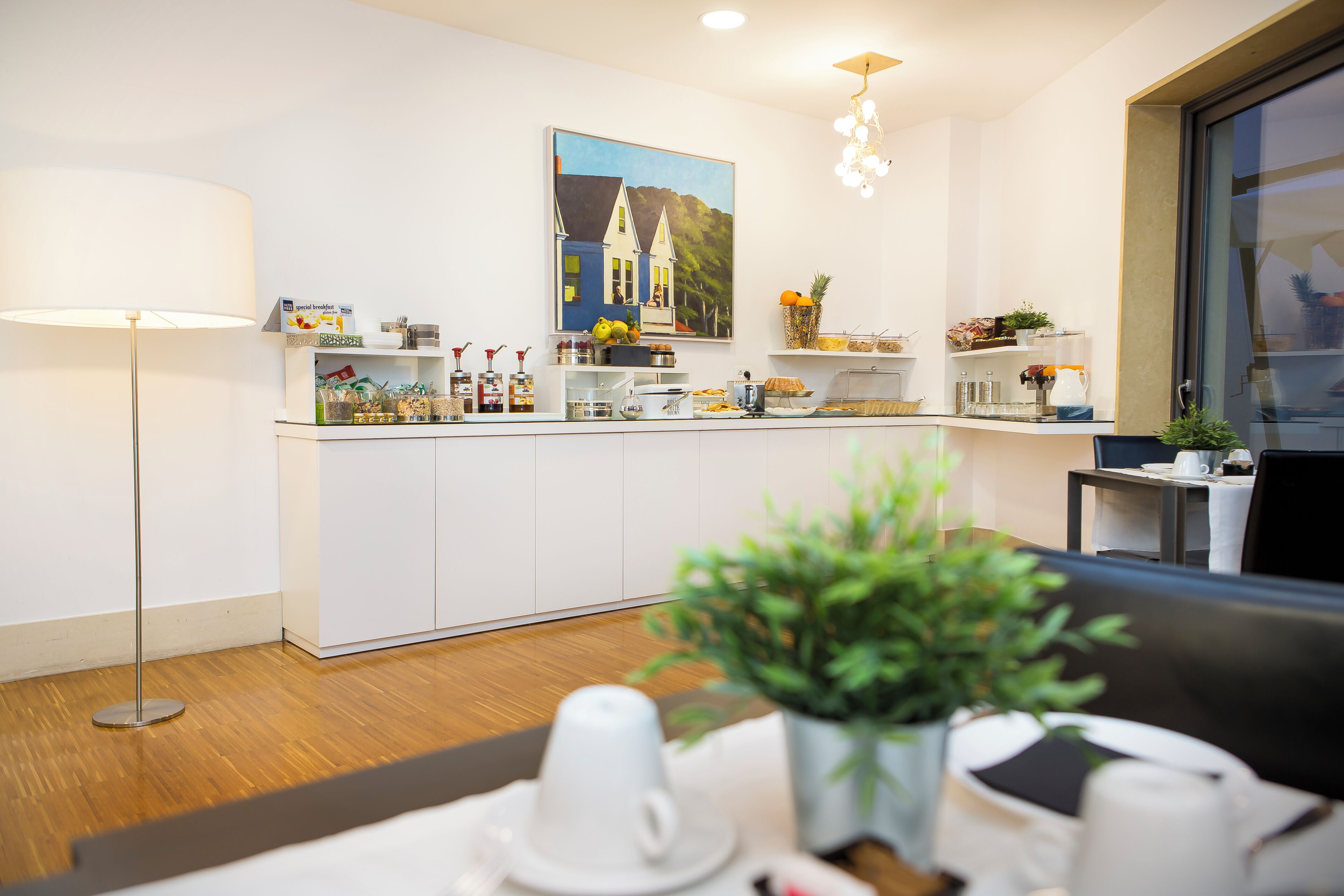 Une cuisine moderne avec des meubles blancs, un tableau au-dessus du plan de travail et un coin repas avec une table et des chaises.