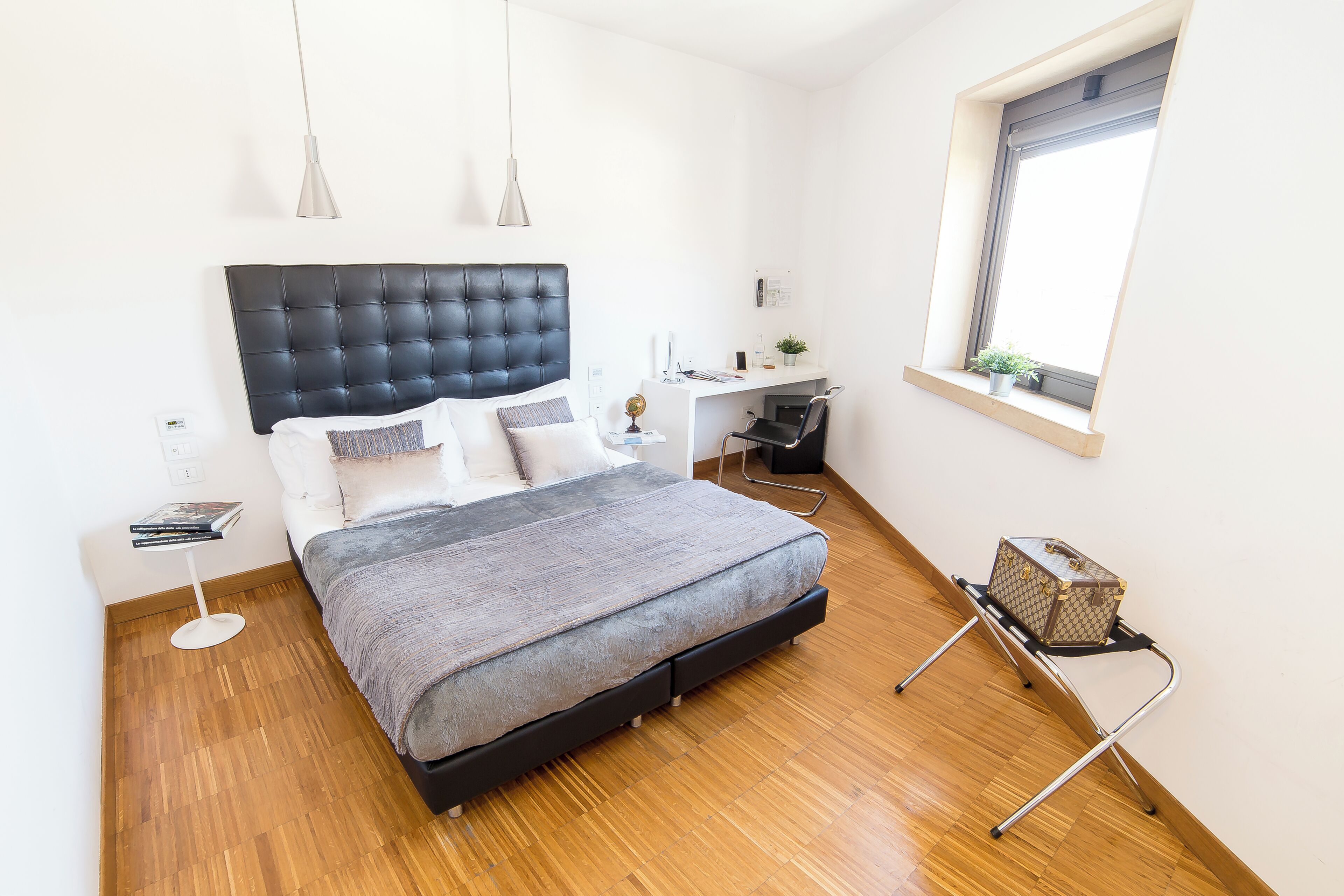 A bedroom with a bed, bedside table, desk, chair, and a window.