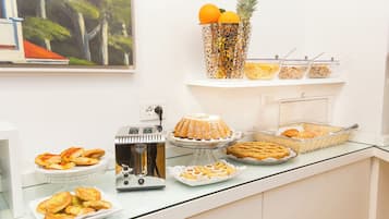 Un bufé con diversos pasteles, una máquina de café y un jarrón decorativo con frutas.