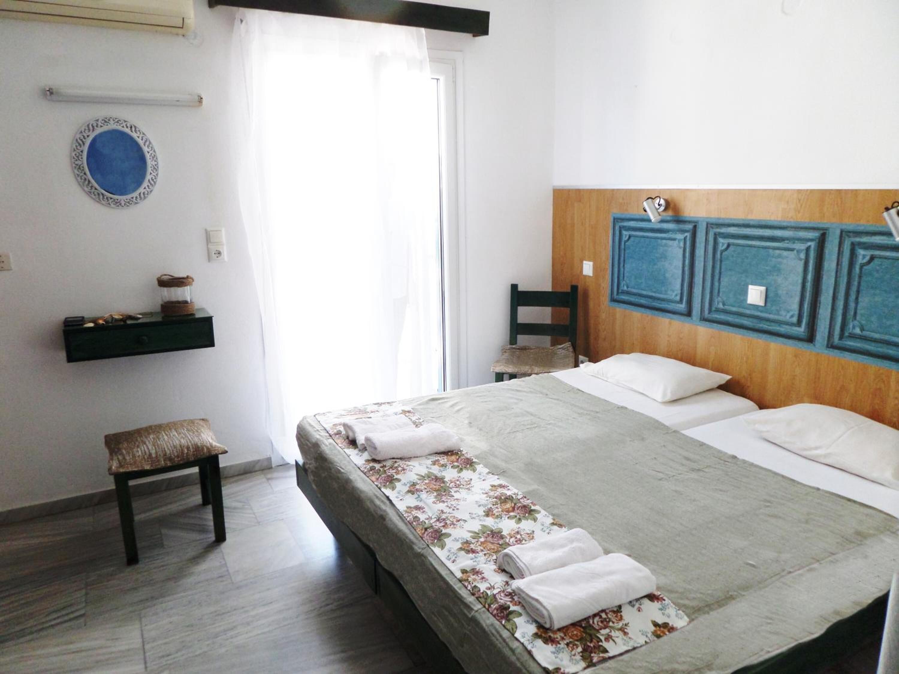 A bedroom with a bed, a chair, a small table with decorative items, and a wall-mounted shelf.