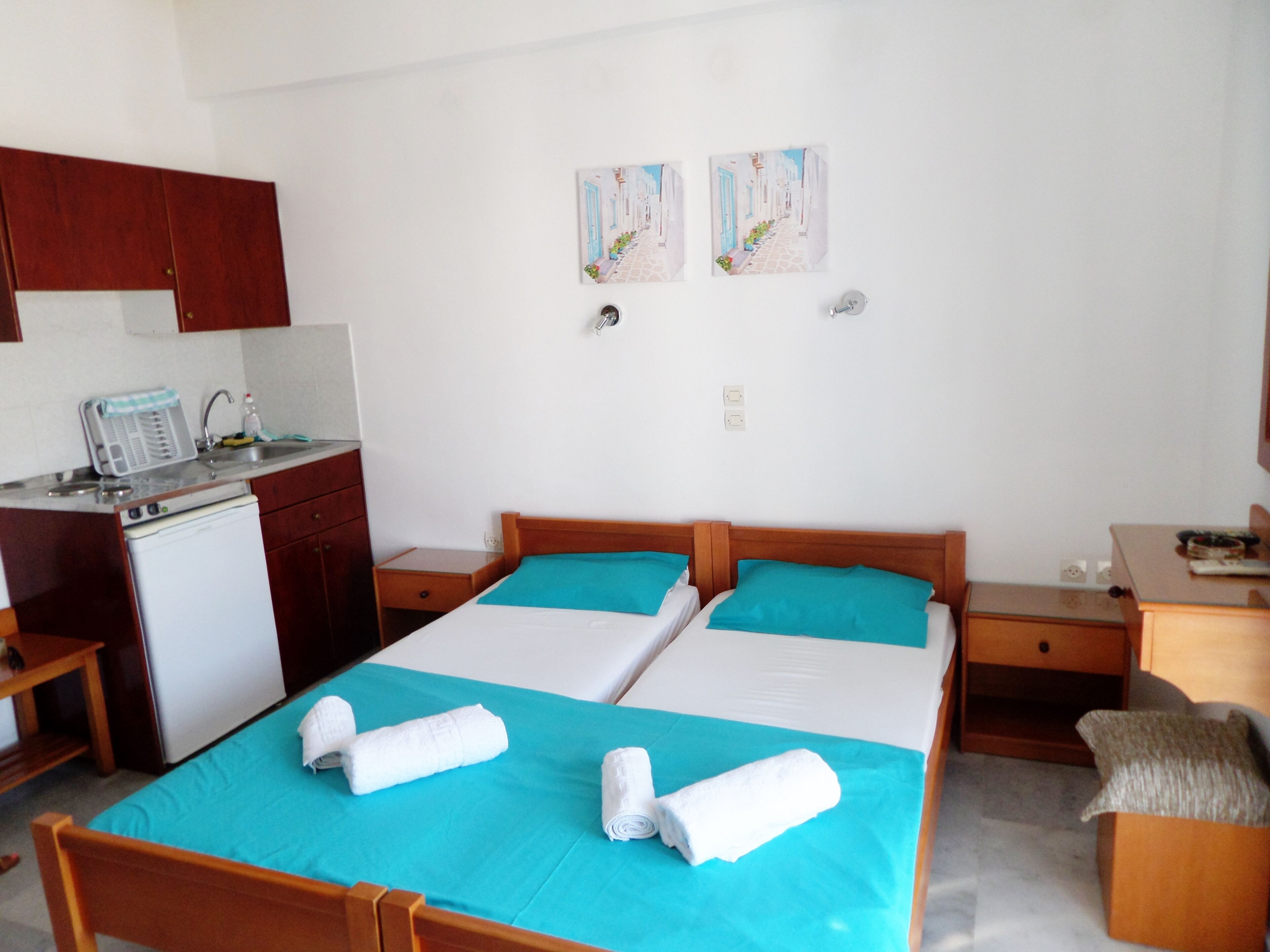 A hotel room with two beds, a kitchenette, and two wall-mounted paintings.