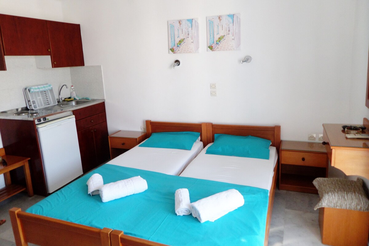 A hotel room with two beds, a small kitchenette, and a bathroom.