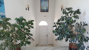 A hallway with a white door, two wall-mounted light fixtures, and two potted plants on either side. - Hotel Rea (Naxos)